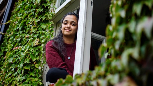Student living in University Housing, sitting in her window looking at the camera.